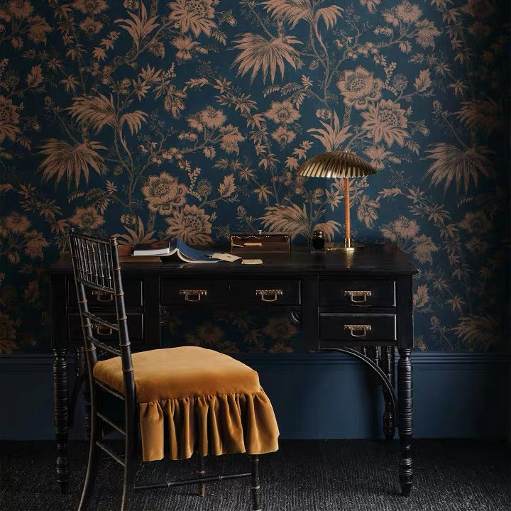 Dark wooden desk with a lamp and chair against floral-patterned wallpaper