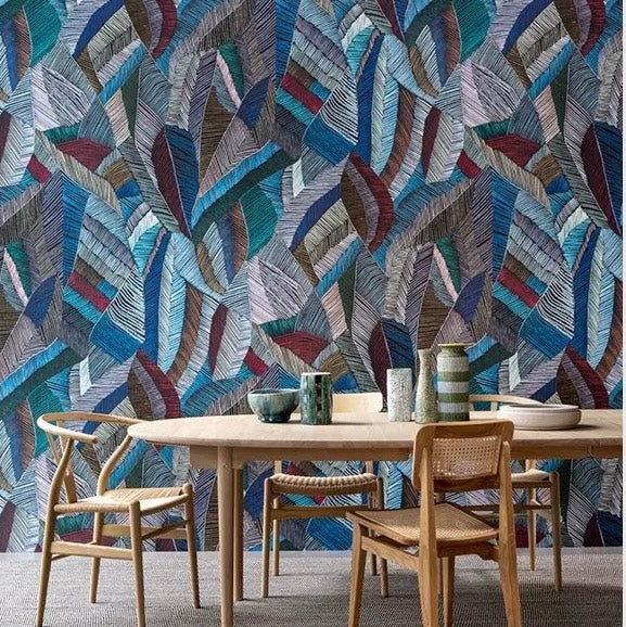 Dining area with a round wooden table and chairs against a colorful leaf patterned wall.